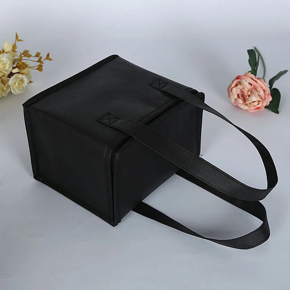 Black handbag with a strap on a light gray background with flowers.