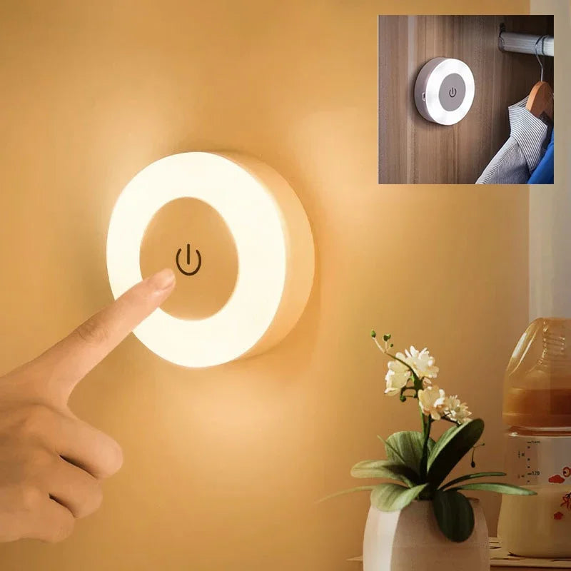 Round wall light with power symbol, hand pressing it, plant, and coffee maker in the background.