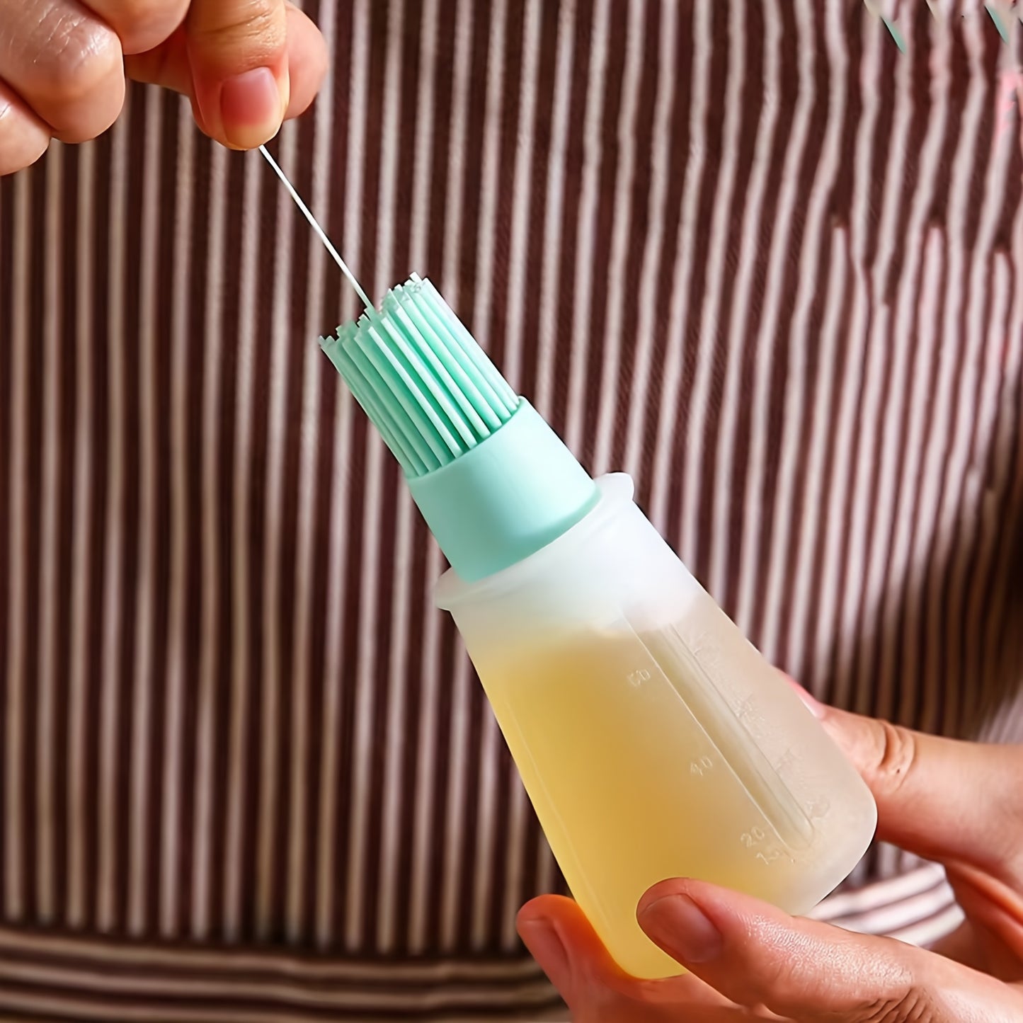 Person holding a bottle with a green brush top, filled with a yellow liquid.
