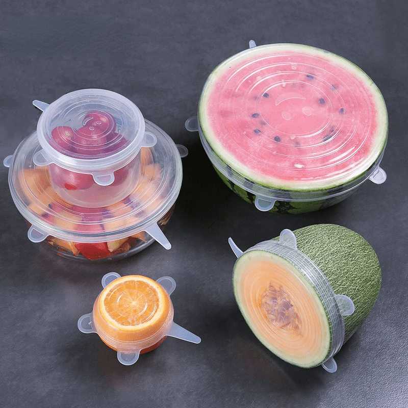 Set of silicone fruit covers on watermelon, cantaloupe, and oranges on a dark surface
