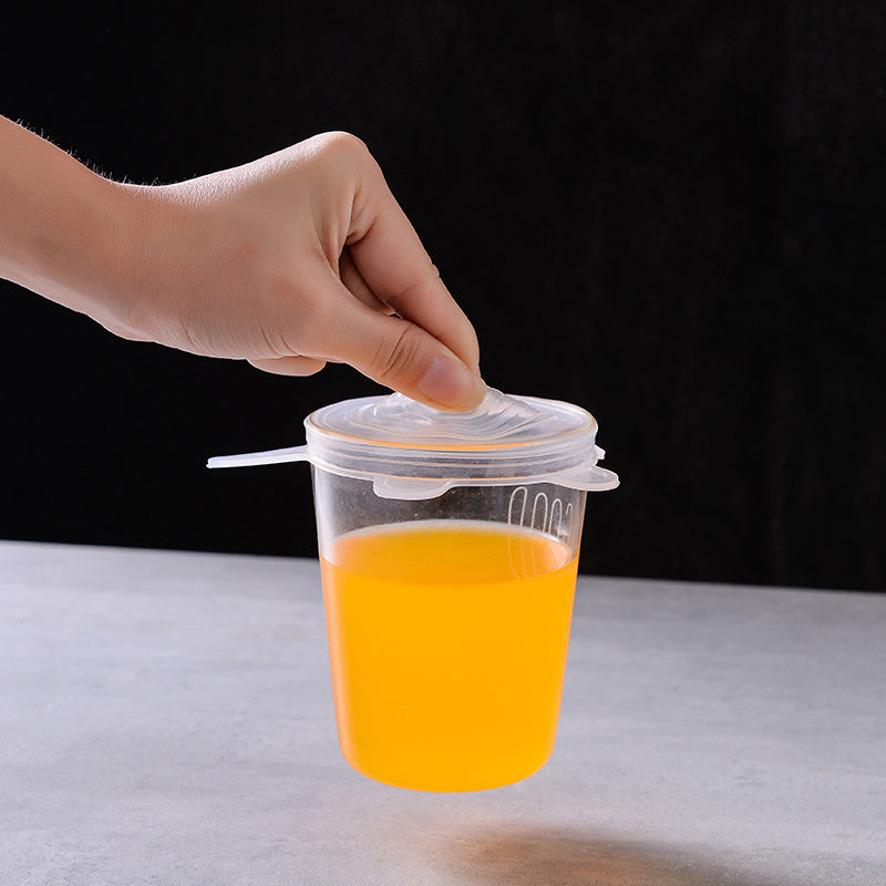 Hand placing a lid on a clear plastic cup filled with orange juice on a light surface.