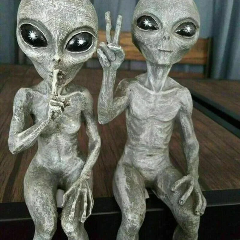 Two gray alien figurines on a wooden surface