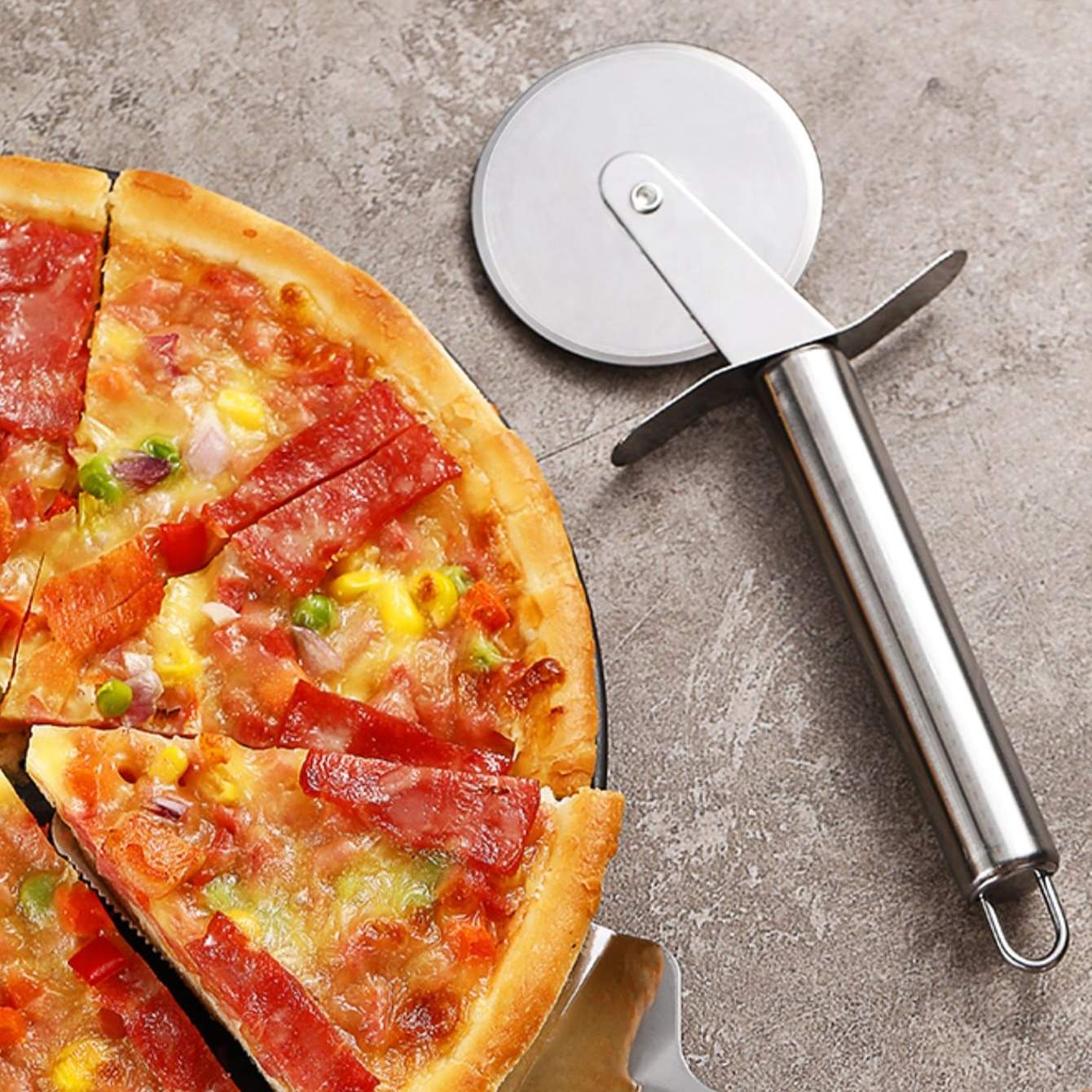 Pizza with various toppings and a pizza cutter on a concrete surface