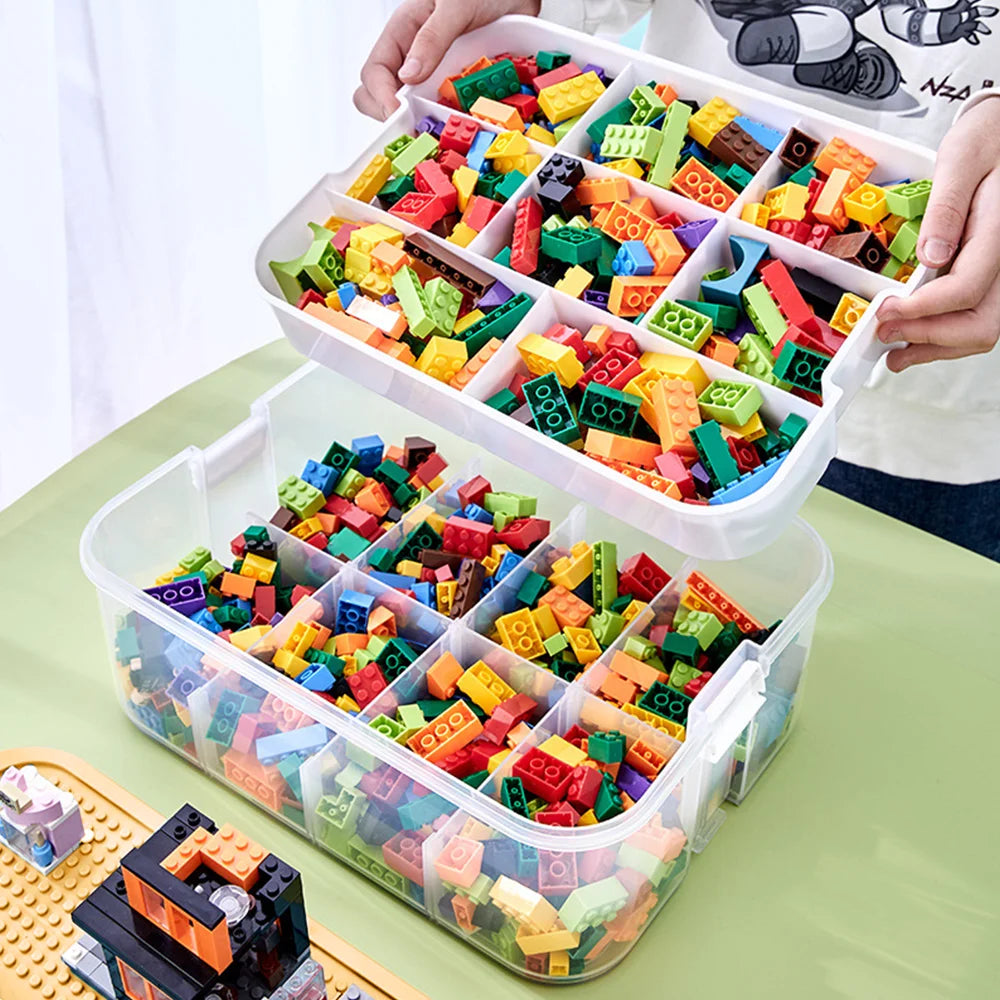 Colorful building blocks in a clear storage container with compartments on a green surface.