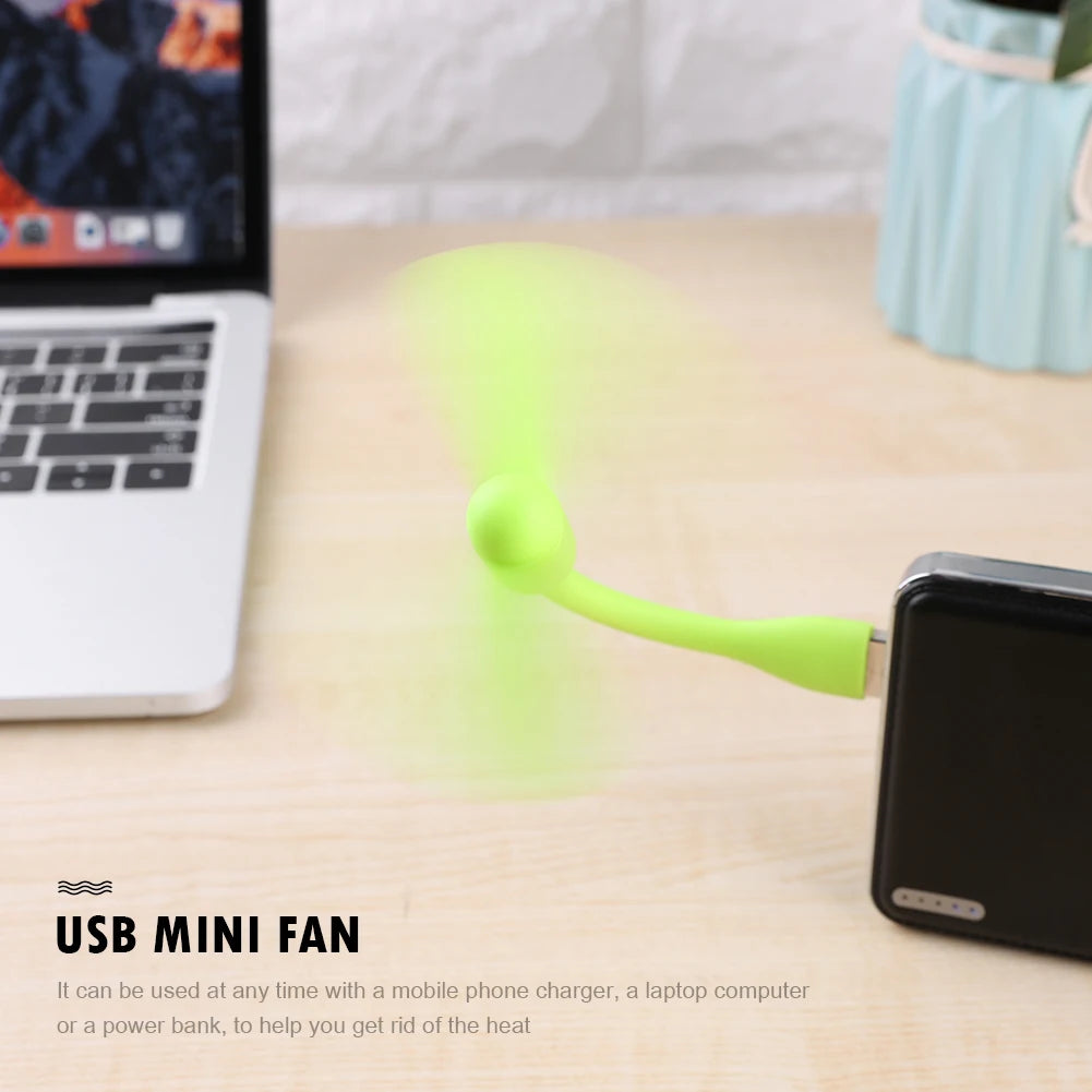 USB mini fan blowing air next to a smartphone and laptop on a desk.