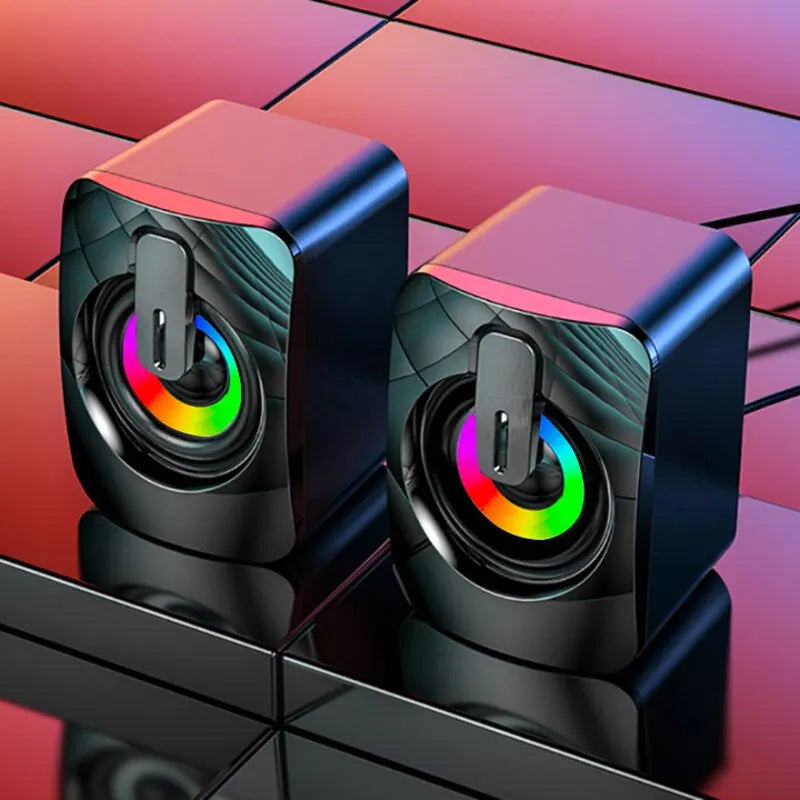 Two black cube-shaped speakers with colorful LED lights on a reflective surface.
