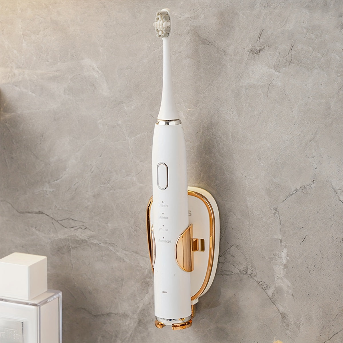 White and gold electric toothbrush mounted on a gray marble wall