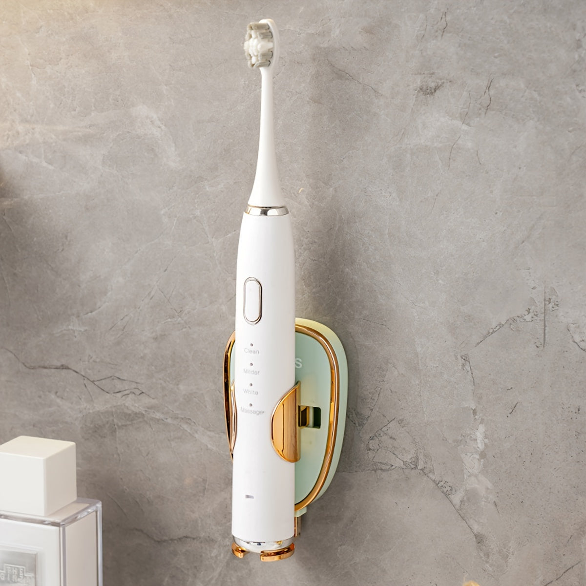 White and gold electric toothbrush on a gray wall-mounted holder