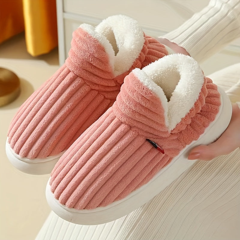Pink slippers with white fur lining held by a hand on a light wooden floor.