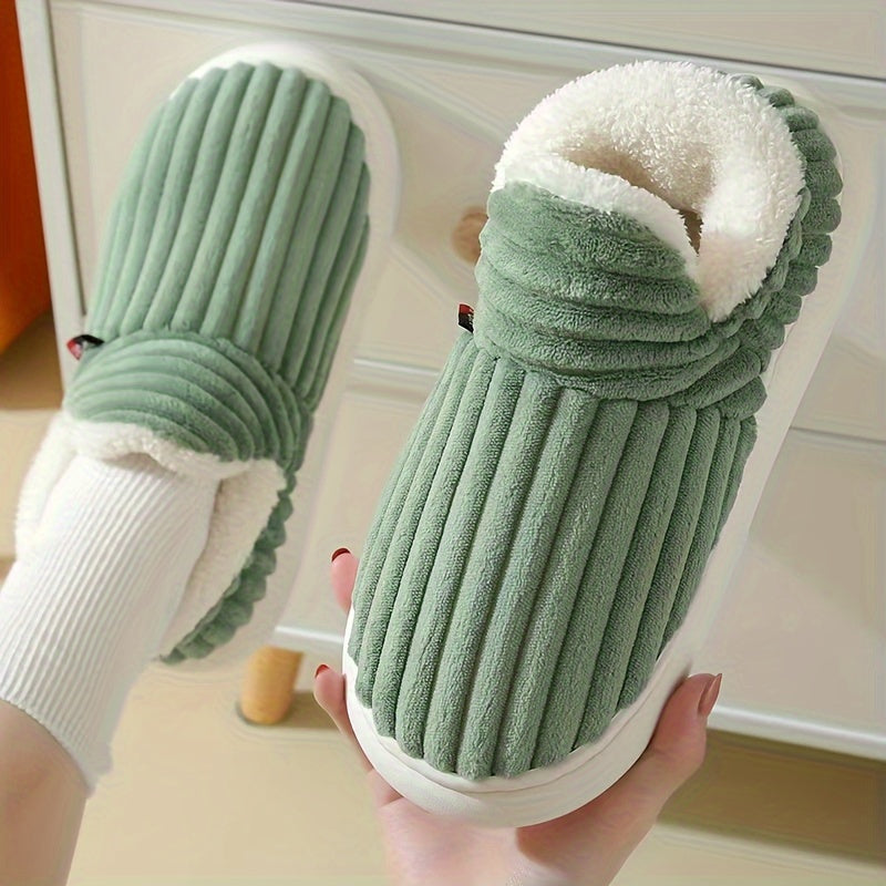 Green slippers with white soles held by a hand against a neutral background