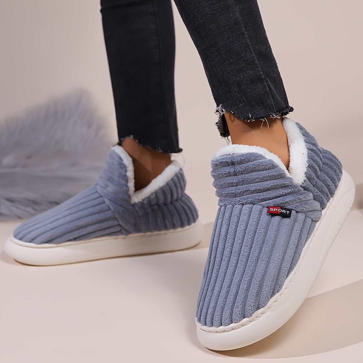 Blue slippers with white soles worn by a person on a neutral background