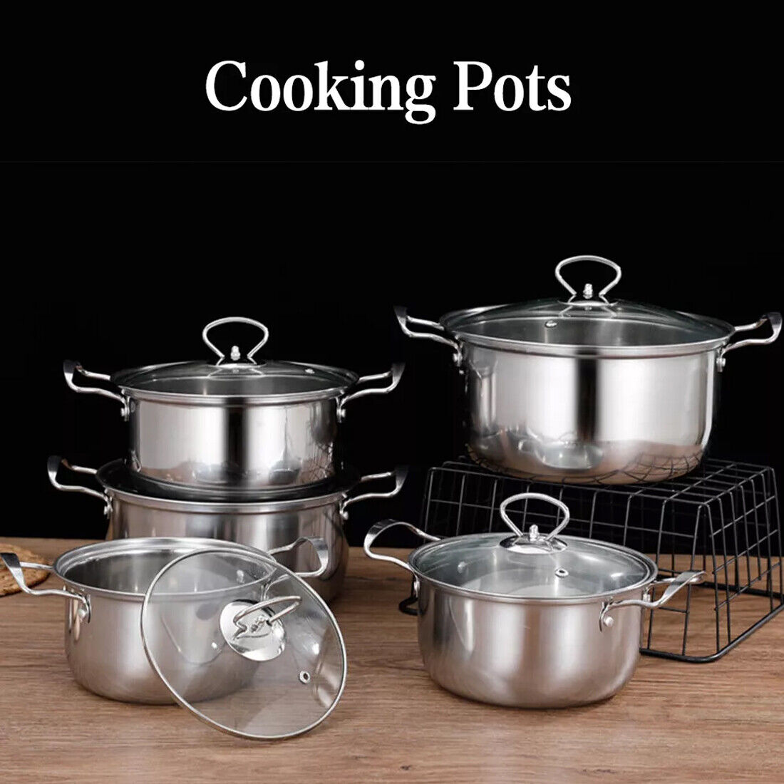 Set of stainless steel cooking pots with lids on a wooden surface.