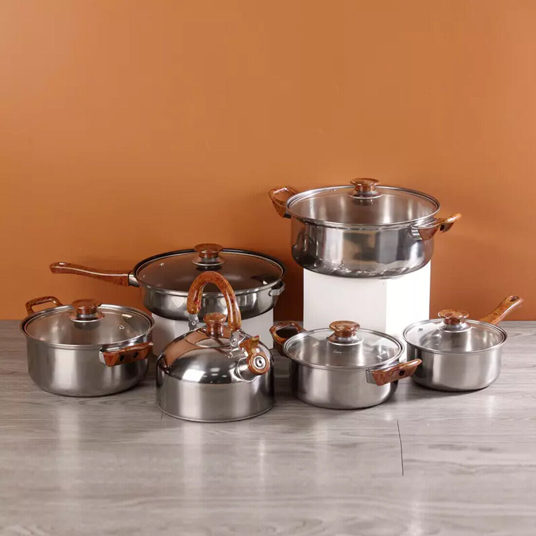 Set of stainless steel cookware with copper handles on a marble surface against an orange wall.