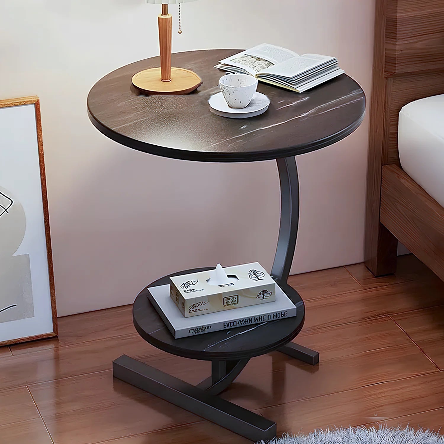 Round wooden side table with a smaller round table on top, featuring a cup, saucer, and books in a bedroom setting.