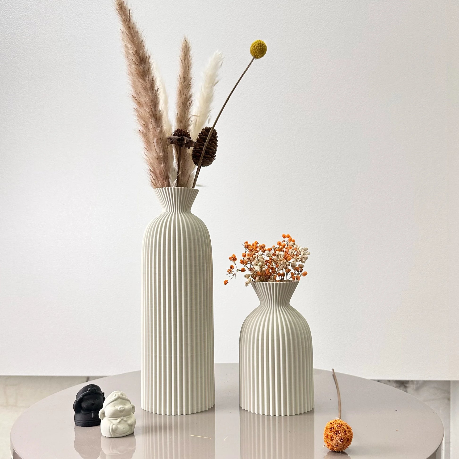 Two decorative vases with dried plants on a white surface