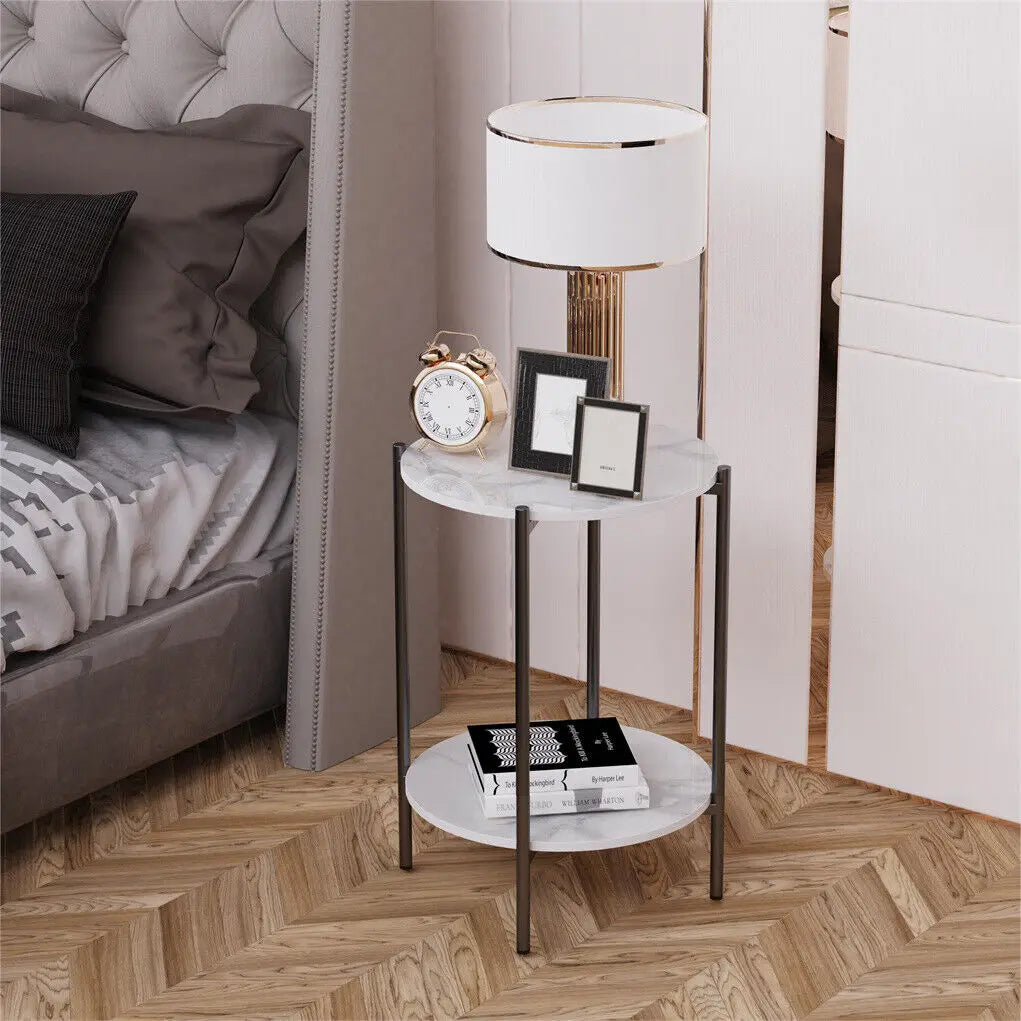 Small marble side table with a lamp, clock, and books next to a bed.