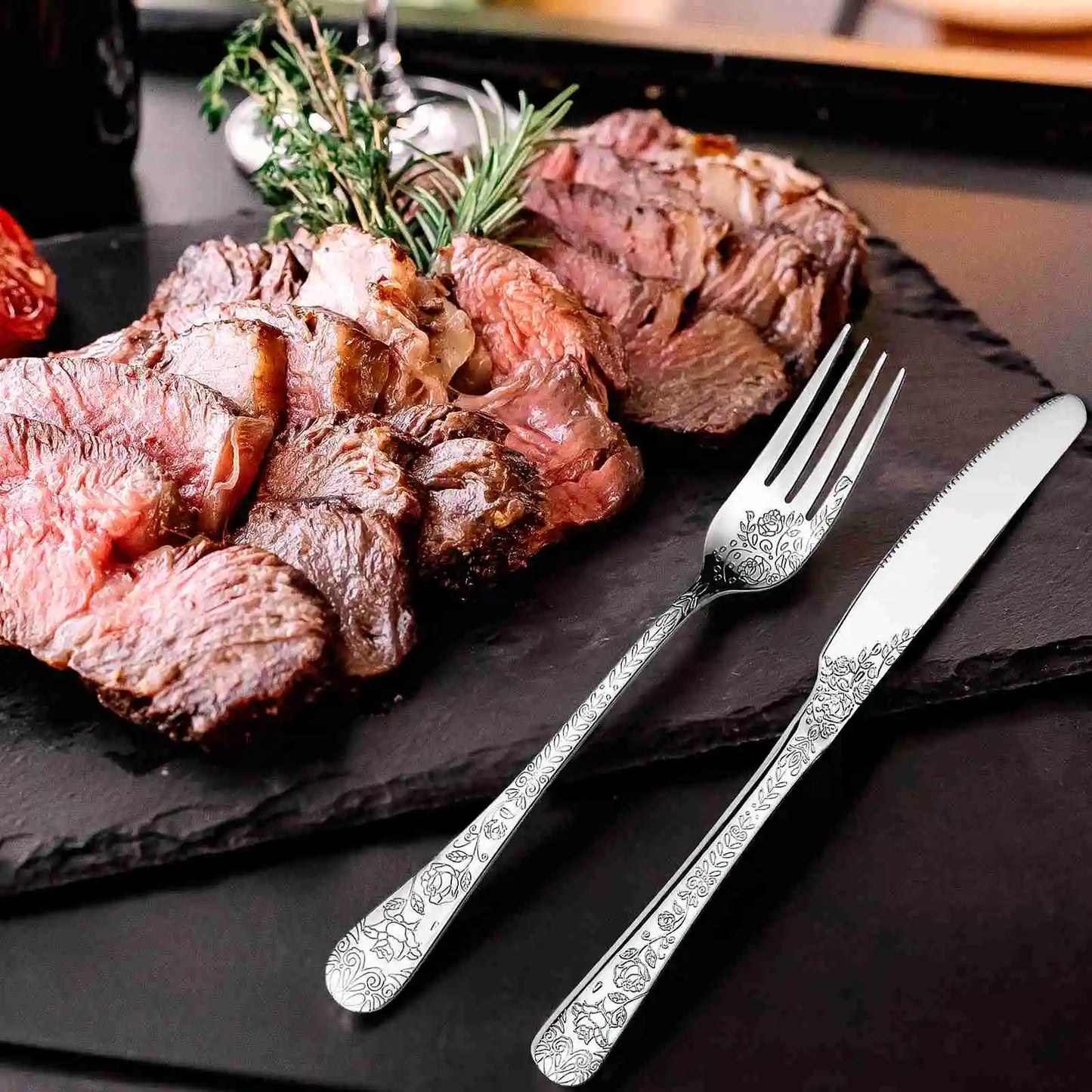 Sliced steak on a black slate with decorative silver fork and knife.