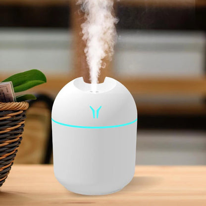 White humidifier with blue light on a wooden surface, emitting mist.