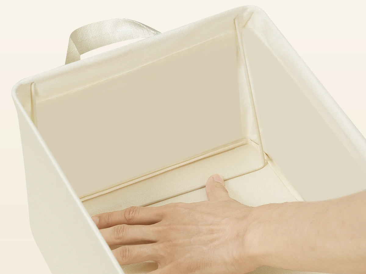 Hand opening a beige fabric storage box on a light beige background