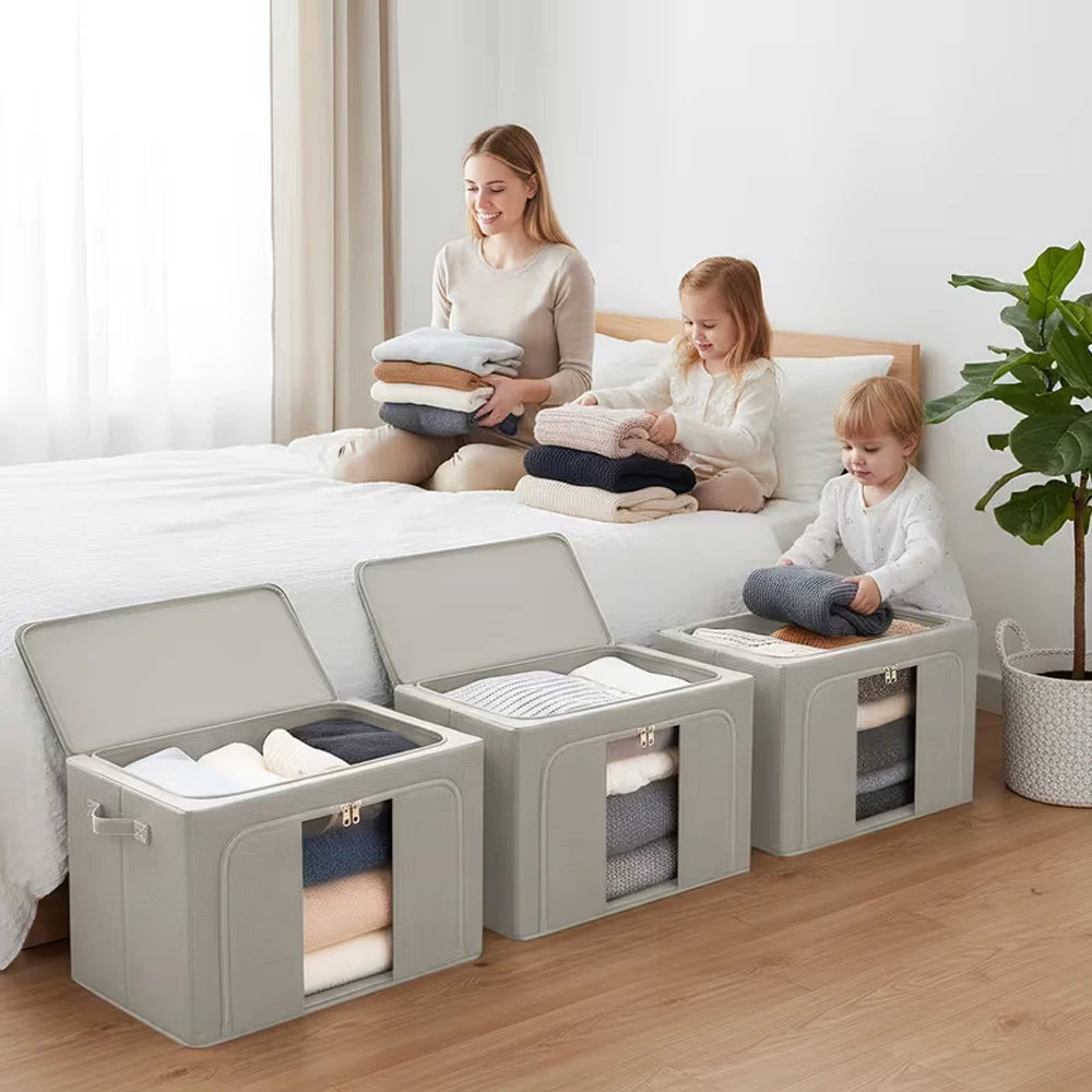 Woman and children sitting on a bed with folded clothes, surrounded by gray storage bins.