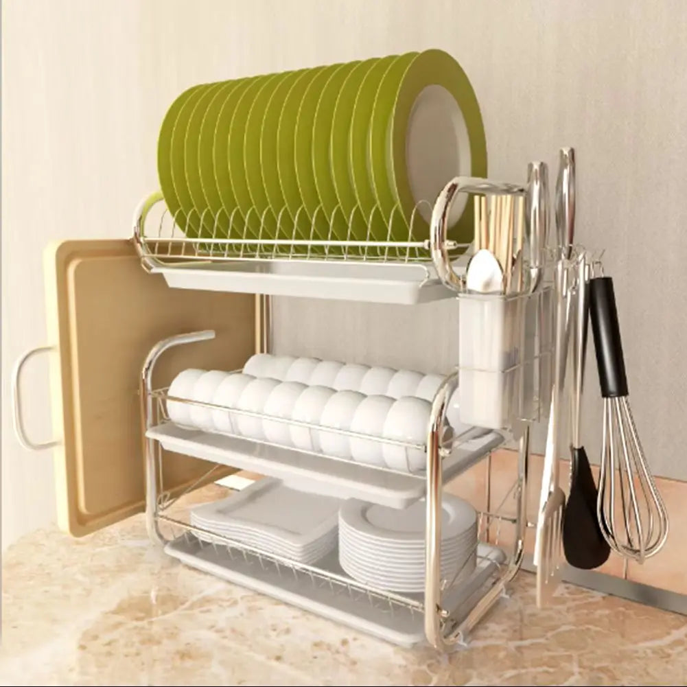 Dish rack with green plates, white cups, and kitchen utensils on a beige countertop.