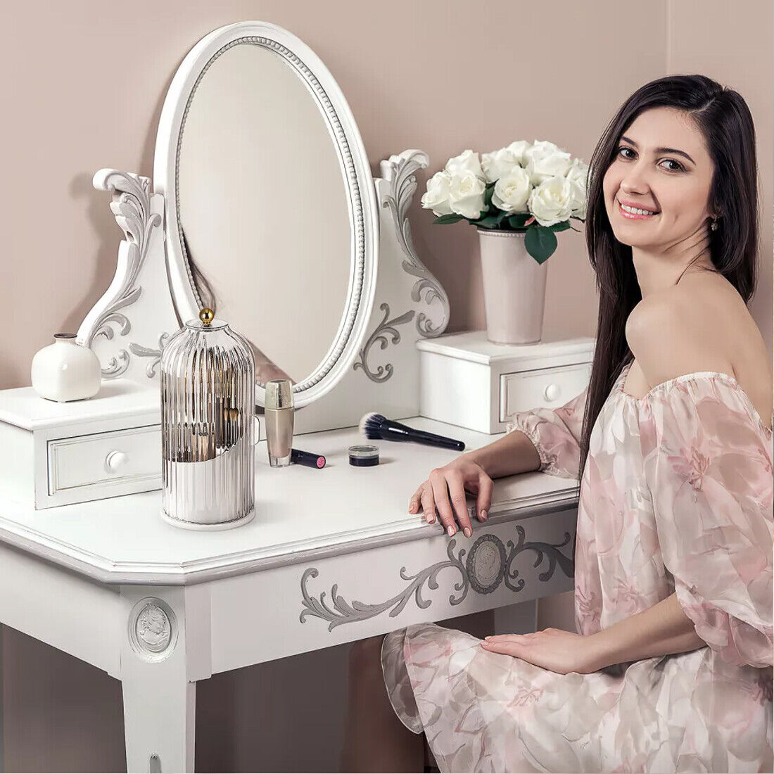 Woman sitting at a white vanity table with decorative mirror and flowers.