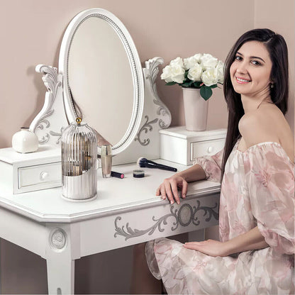 Woman sitting at a white vanity table with decorative mirror and flowers.
