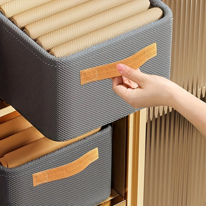 Gray woven storage bins with brown handles being held by a hand against a neutral background