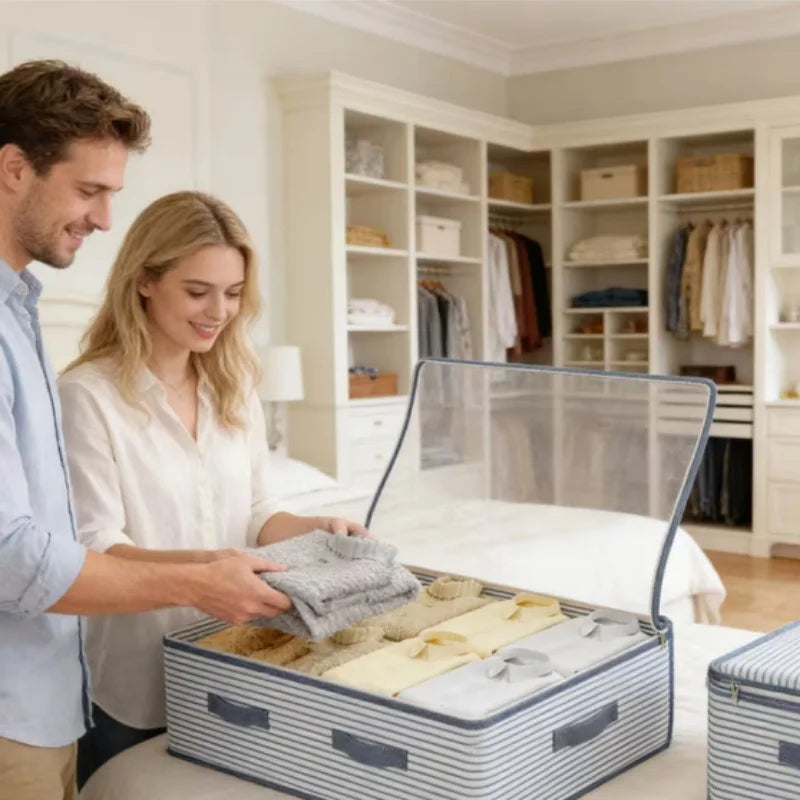 A man and a woman packing clothes into a striped fabric storage suitcase with a clear lid in a bright, modern bedroom.