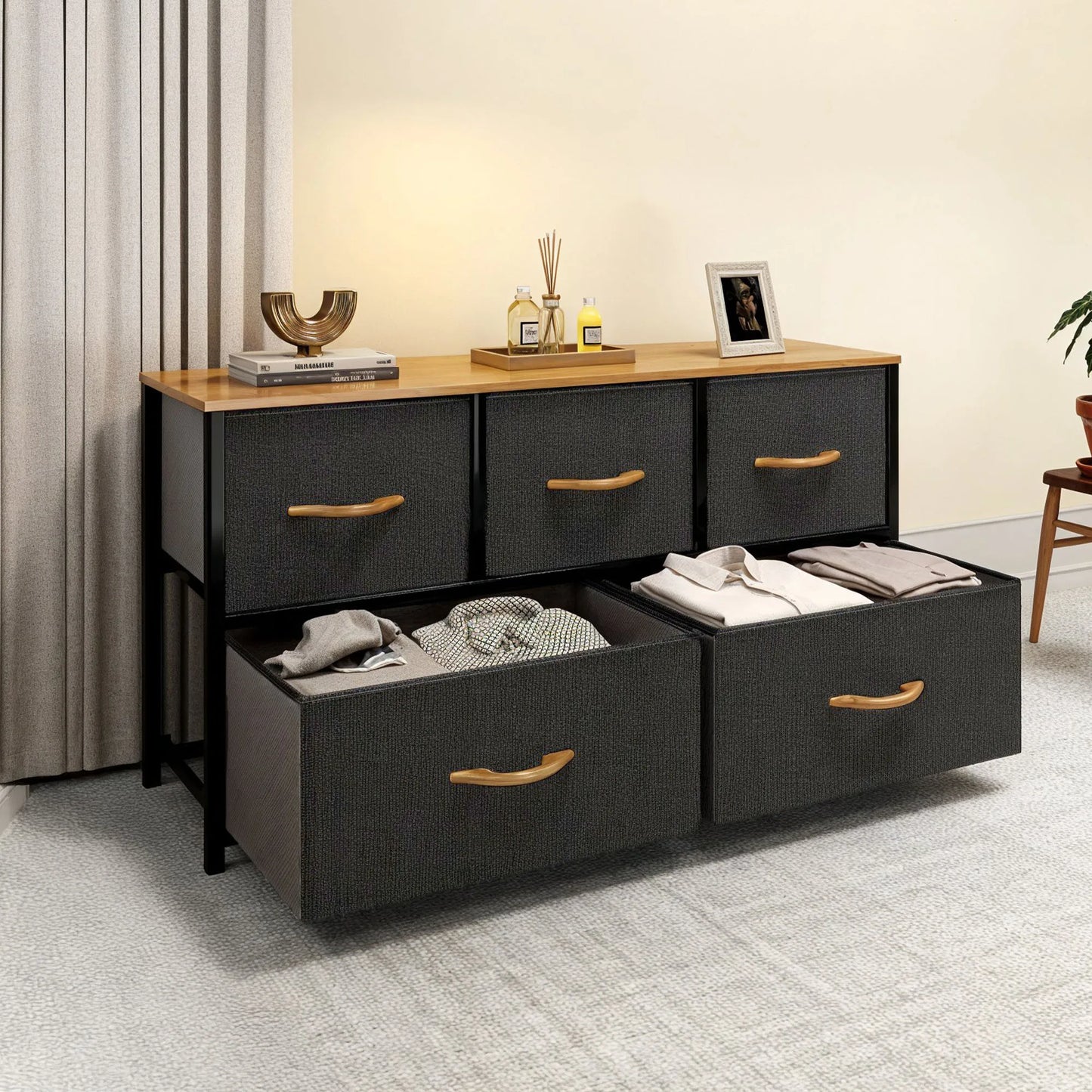 Black dresser with open drawers containing clothes, on a light gray floor with a neutral-colored wall background.
