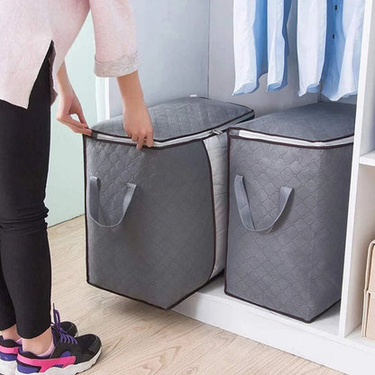 Person holding a gray quilted storage bag next to another similar bag in a room with clothes on a rack.