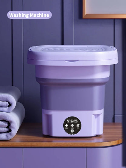 Purple folding washing machine on a wooden surface with a purple wall in the background.