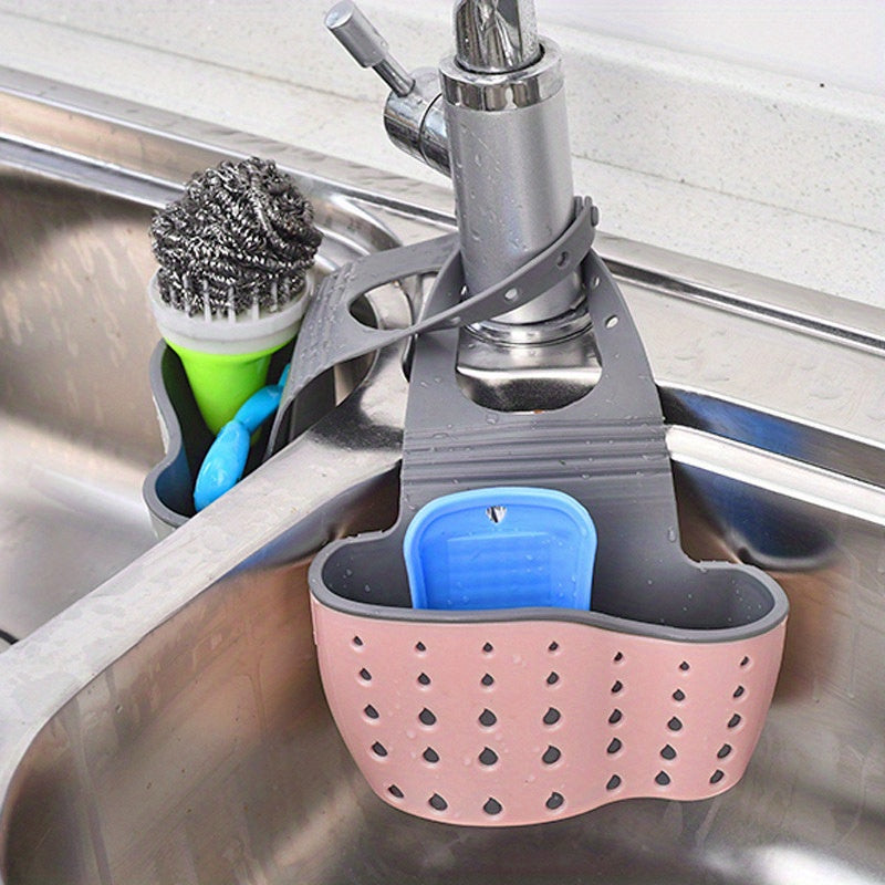 Pink and gray kitchen sink caddy with blue holder hanging on a faucet.