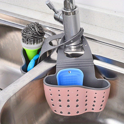 Pink and gray kitchen sink caddy with blue holder hanging on a faucet.