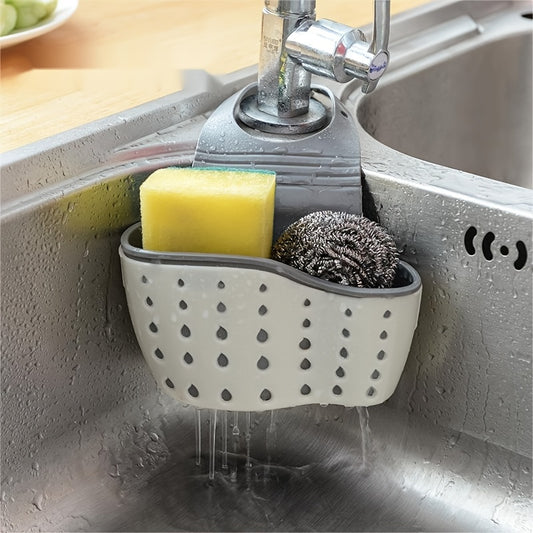 Gray sink caddy with sponge and scrubber hanging over a running faucet in a kitchen.