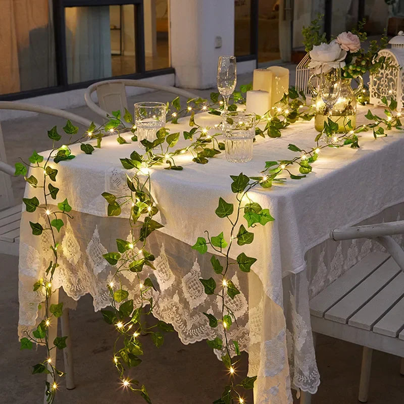 Decorated table with string lights, greenery, and candles in an outdoor setting.