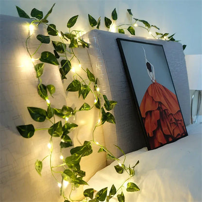 Decorative string lights with green leaves draped over a bookshelf with a painting on it.