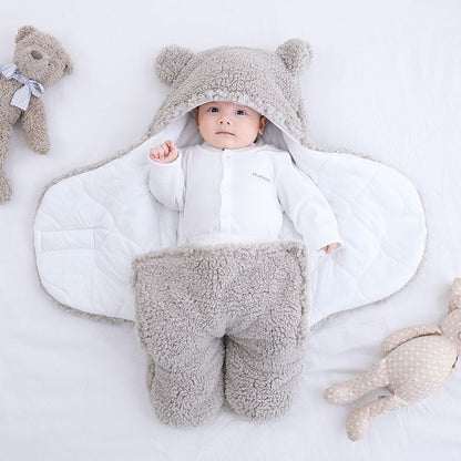 Baby in a white outfit with gray fleece legs and ears, surrounded by teddy bears on a light background