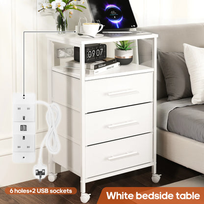 White bedside table with drawers, laptop, alarm clock, and other items in a bedroom setting.