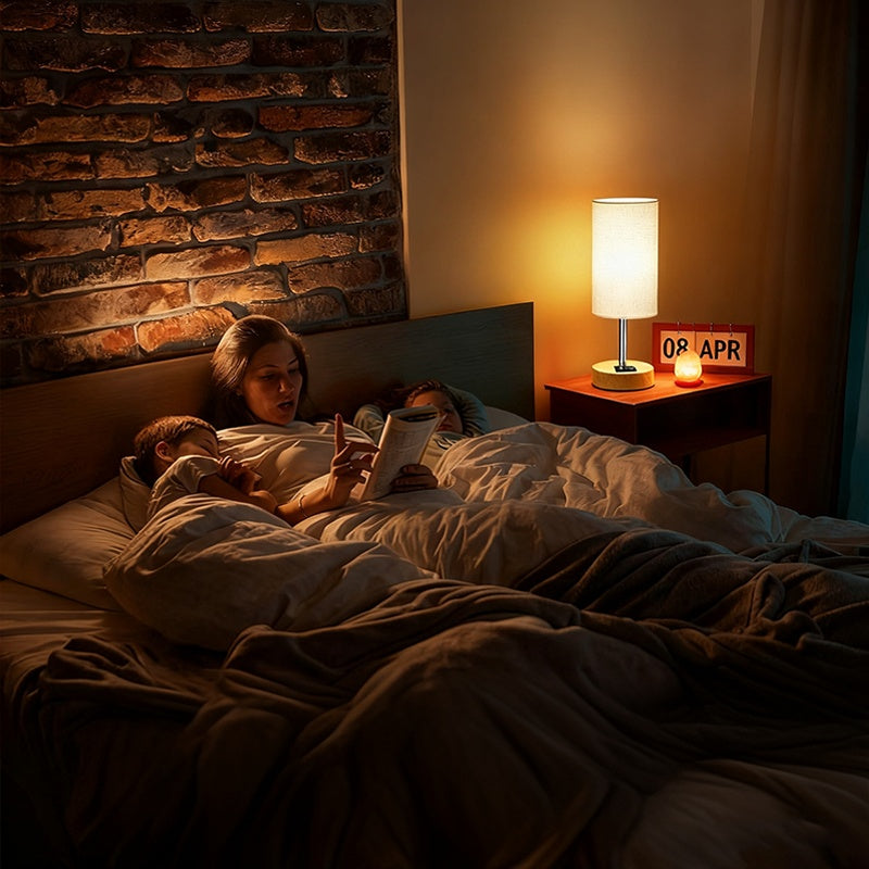 Woman reading a book to a child in bed with a warm lamp on a nightstand.
