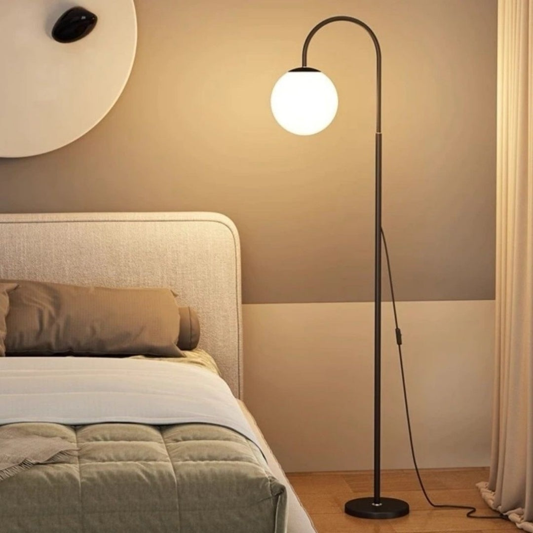 Floor lamp with a round white light bulb in a bedroom setting.
