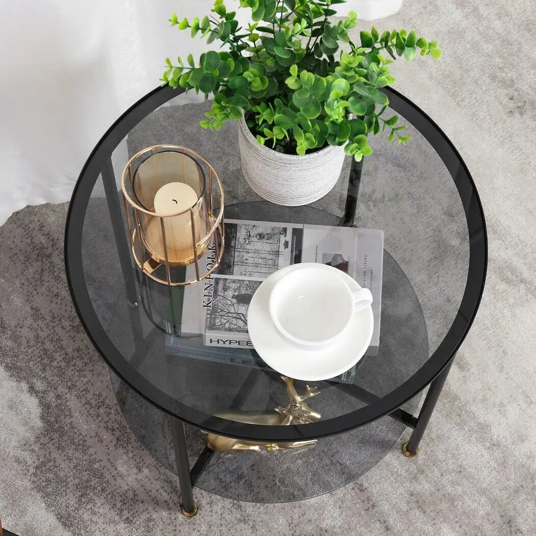 Round glass coffee table with a candle, plant, and newspaper on a gray carpet.