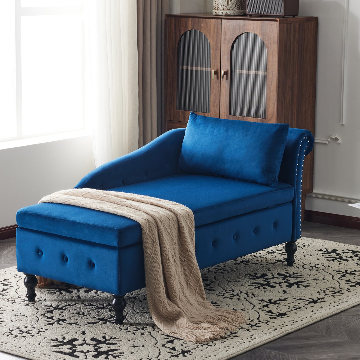 Blue chaise lounge with a beige blanket on a patterned rug in a room with a wooden cabinet.