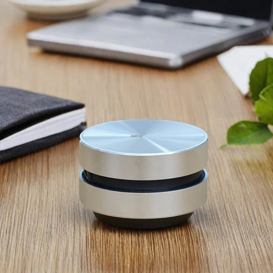 Small round device on a wooden surface with a laptop and notebook in the background