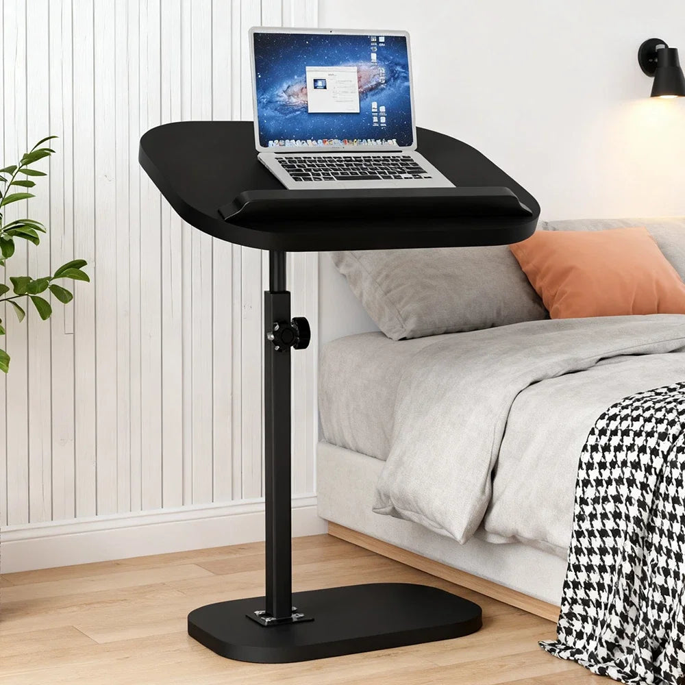 Black adjustable laptop stand on a wooden floor with a bed in the background