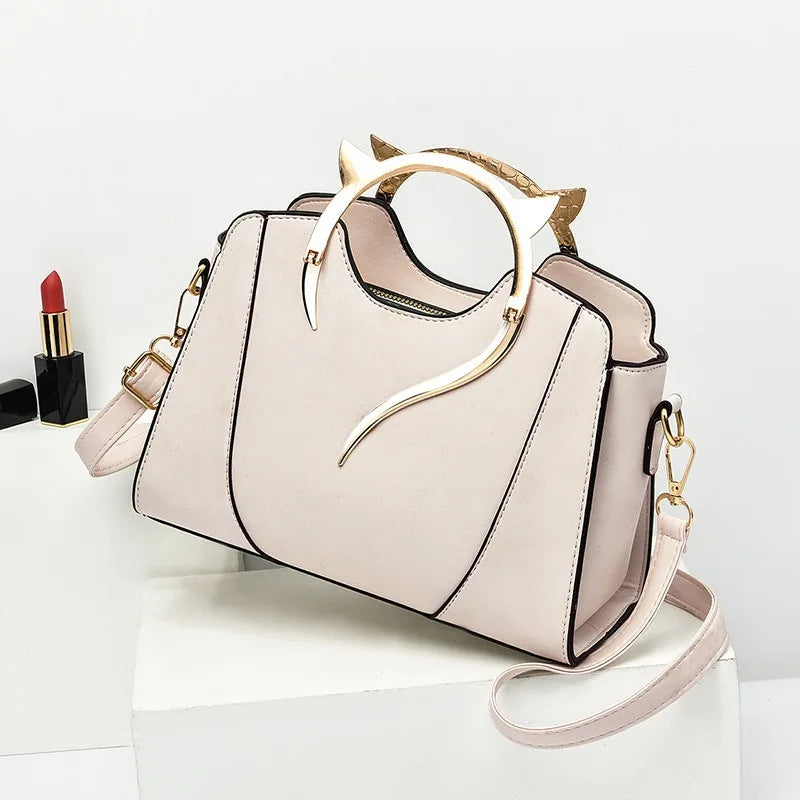 Beige handbag with gold accents on a white surface, next to a red lipstick.