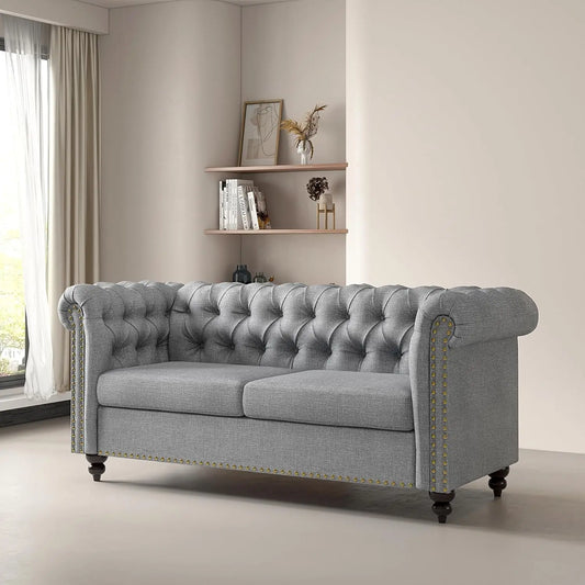 Gray tufted sofa in a living room setting with a shelf in the background.