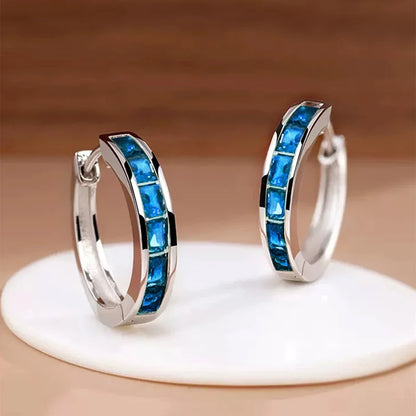 Silver hoop earrings with blue gemstones on a beige background