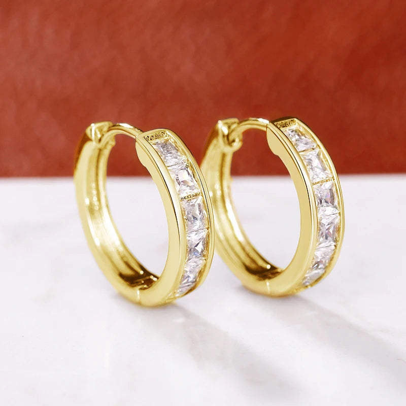 Gold hoop earrings with clear gemstones on a white surface with a red background