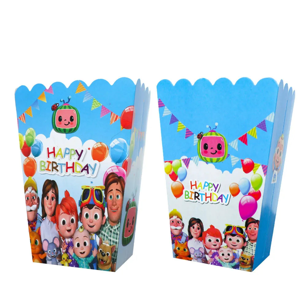 Two blue Cocomico-themed cardboard party boxes with scalloped edges, featuring colorful cartoon characters, balloons, bunting, and 'Happy Birthday' text on a white background.